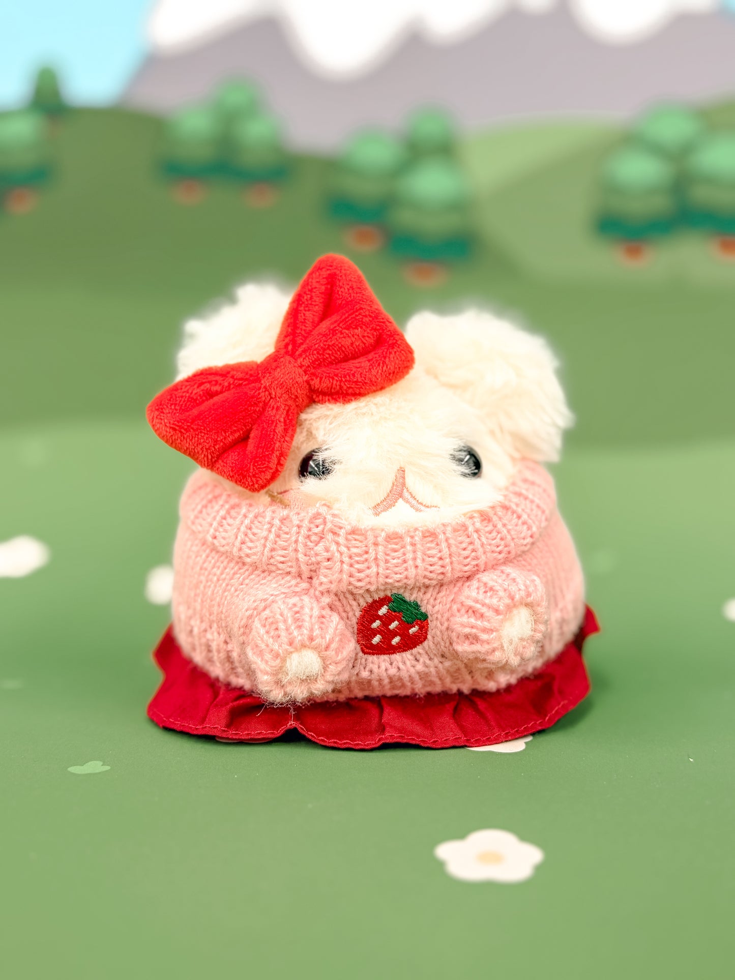 Plush toy Bellinghamster in a pink sweater with a red bow on a green background